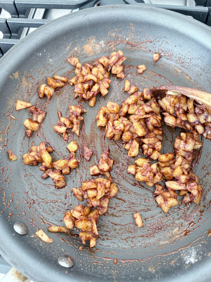 Cinnamon added to cooked apples in a skillet.