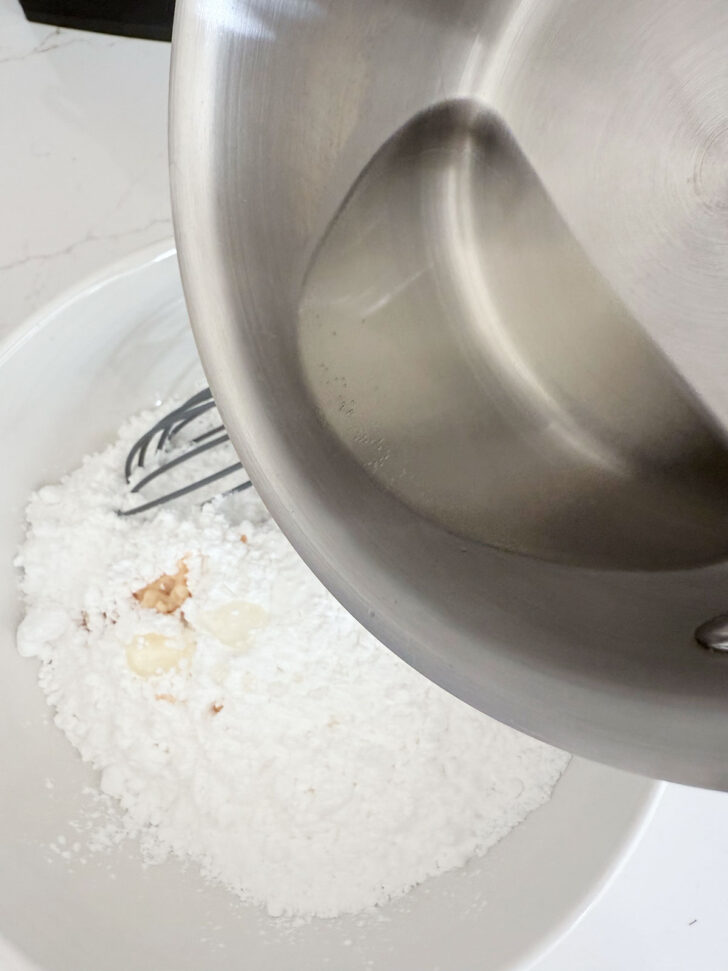 Adding the sugar syrup to the icing sugar in a bowl.