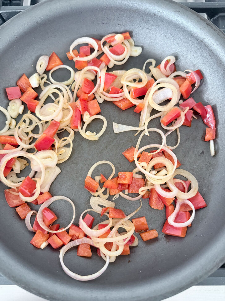 Shallots and bell pepper cooking in a skillet.