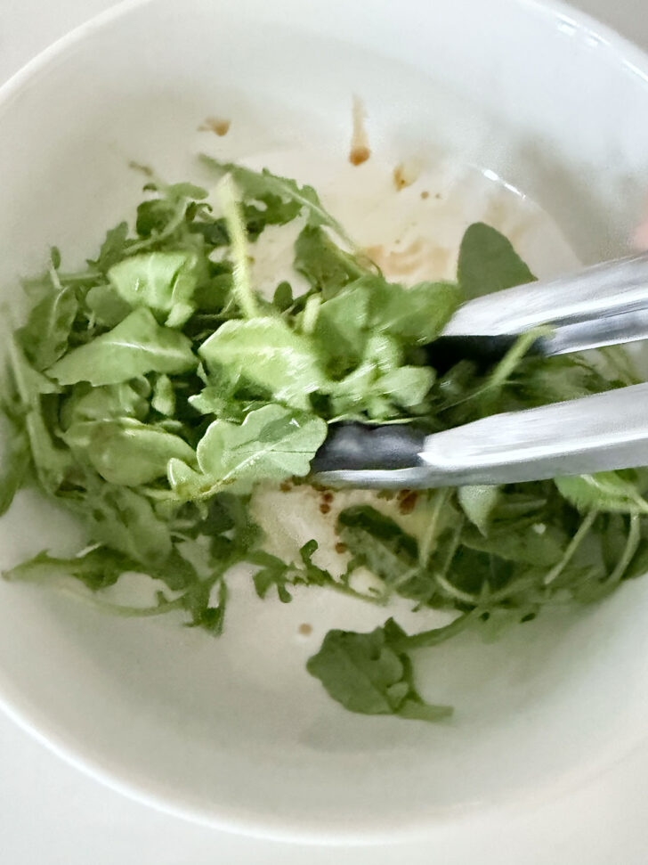 Tossing the arugula topping in a bowl.