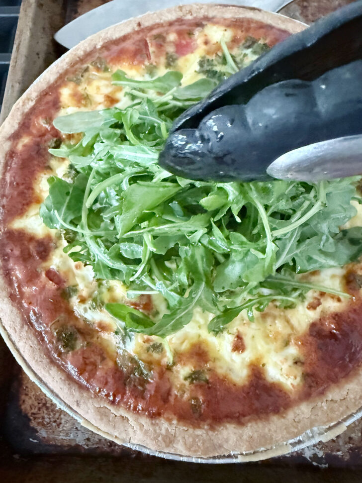 Placing the arugula topping onto the cooked quiche.
