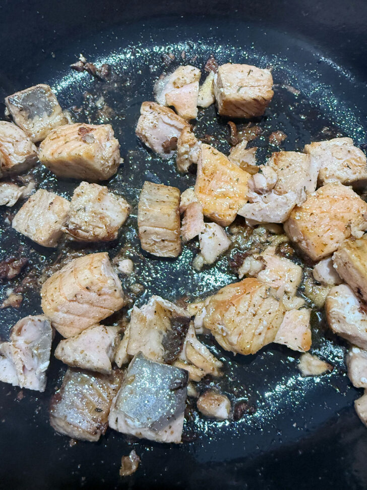 Salmon pieces cooking in a skillet,