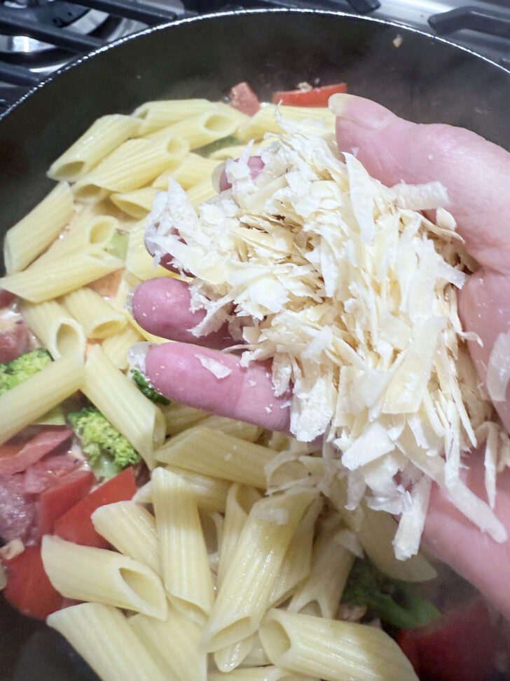 Adding parmesan cheese to the skillet,