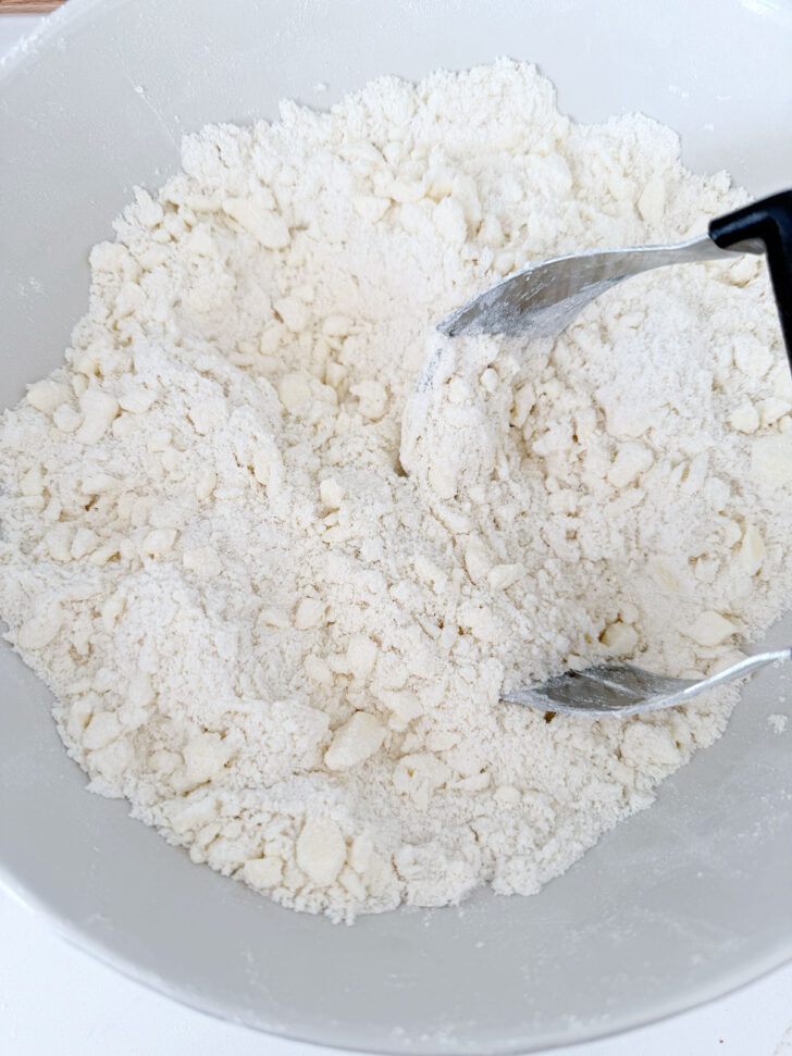 Cutting the butter into the flour mixture with a pastry cutter.