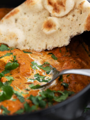 Butter chicken in a skillet with naan bread.