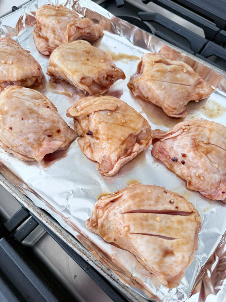 Marinated chicken thighs on a foil-lined baking sheet.