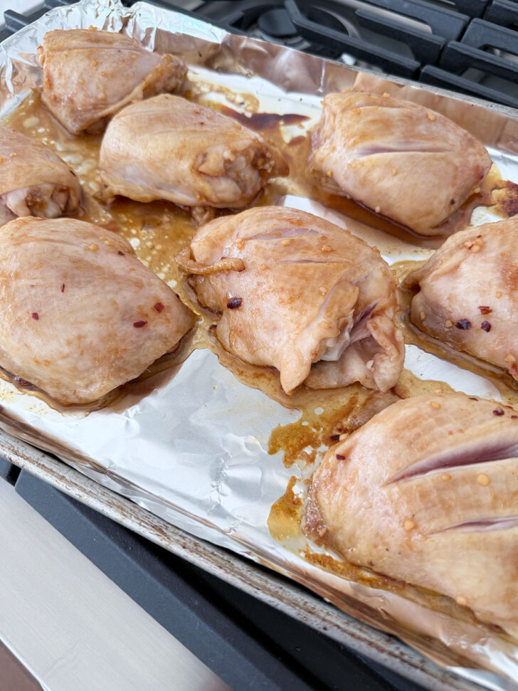 Partially cooked chicken thighs on the baking sheet.