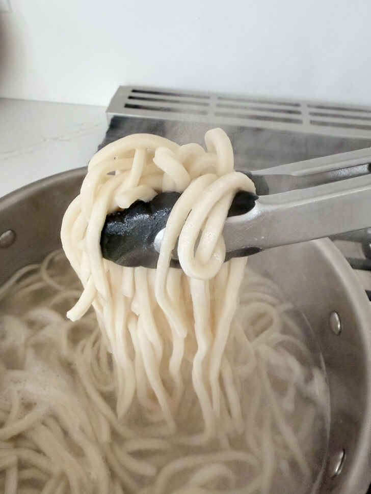 Udon noodles being lifted from boiling water after boiling.