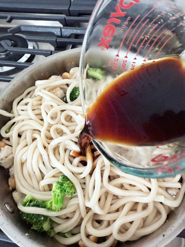Adding the sauce to the skillet with the noodles, chicken, broccoli and cashews.