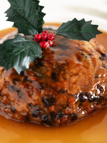Christmas pudding with rum sauce on a serving plate.