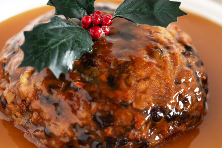Christmas pudding with rum sauce on a serving plate.