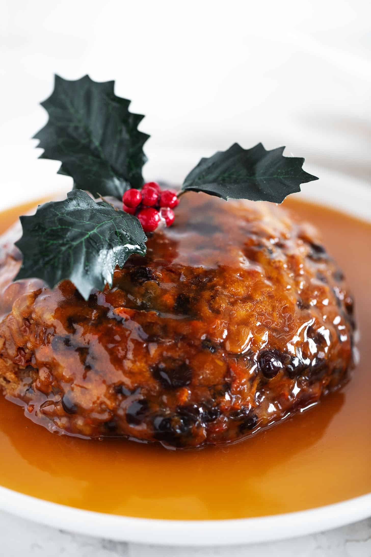 Christmas pudding on a serving plate with rum sauce overtop.