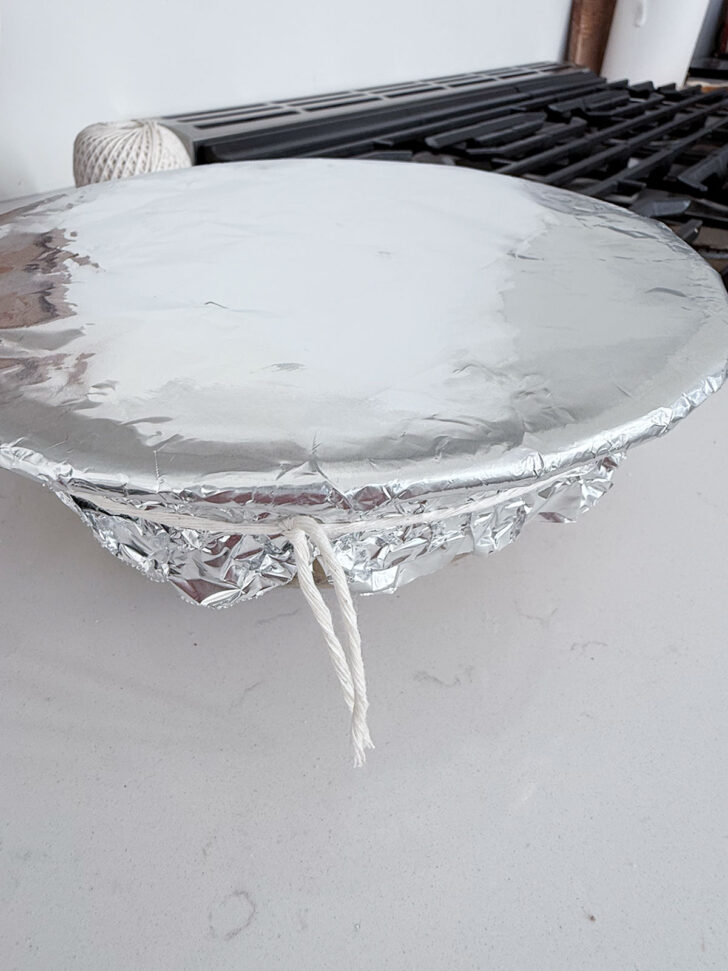 Pudding covered with parchment and foil and tied closed.