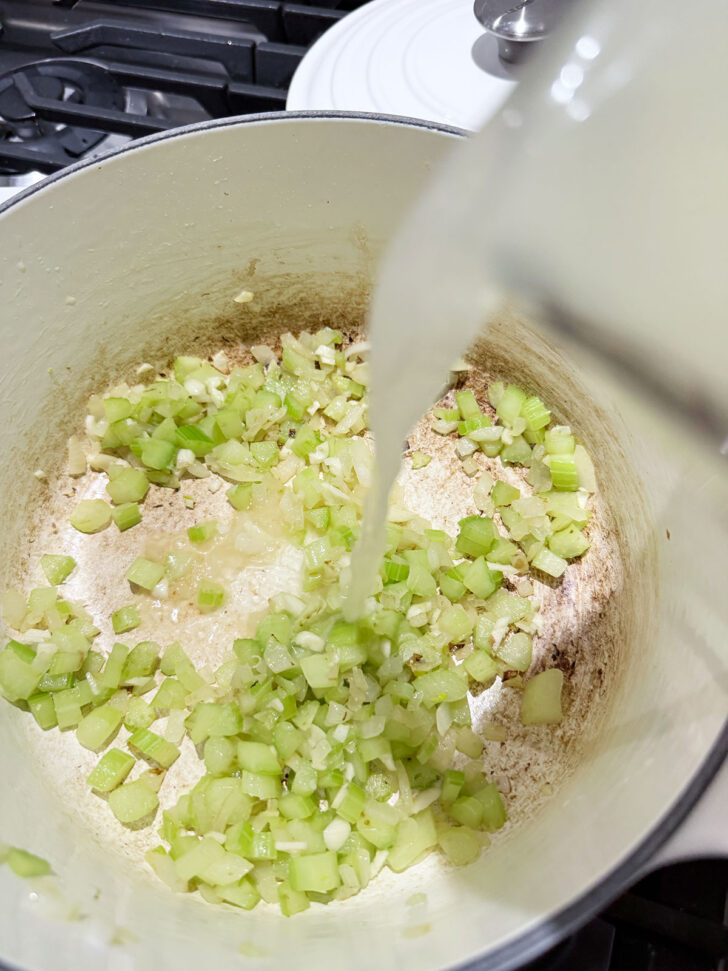 Adding broth to the cooked onion and celery in a soup pot.