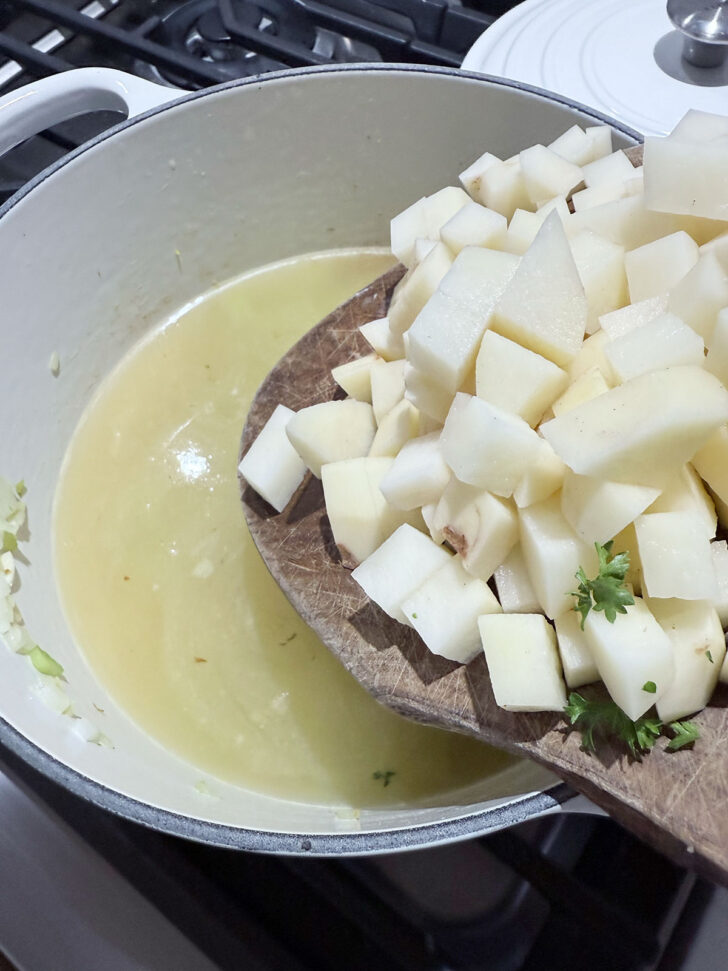 Adding diced potatoes to the soup pot.