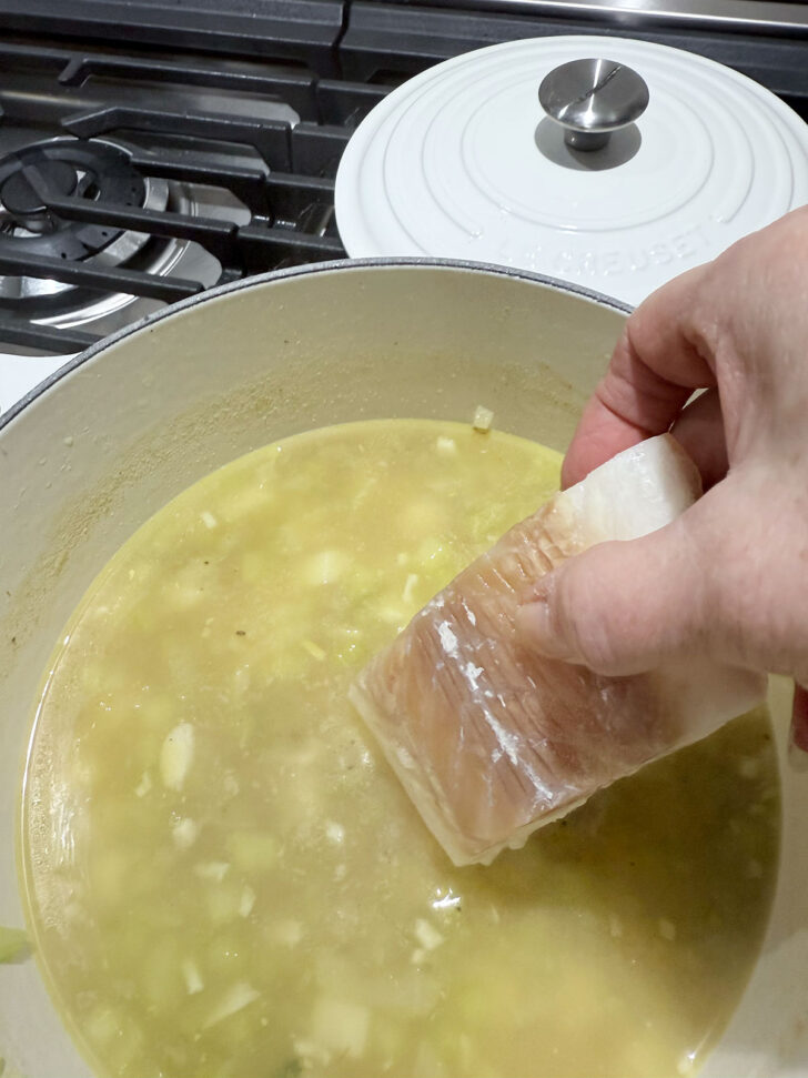 Adding frozen cod pieces to the simmering chowder.