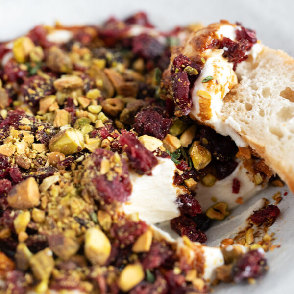 Cranberry balsamic topped whipped ricotta in a bowl with a baguette slice.