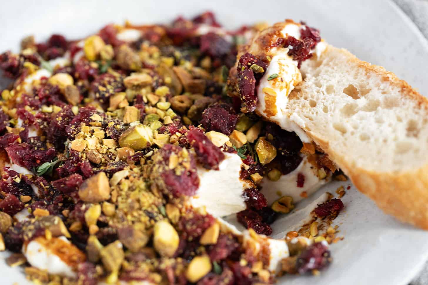 Cranberry balsamic topped whipped ricotta in a bowl with a baguette slice.