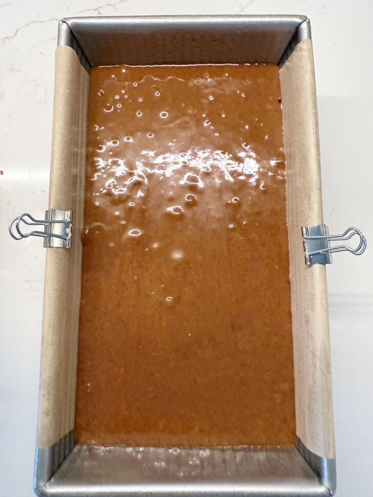 Gingerbread loaf batter added to a parchment-lined loaf pan.
