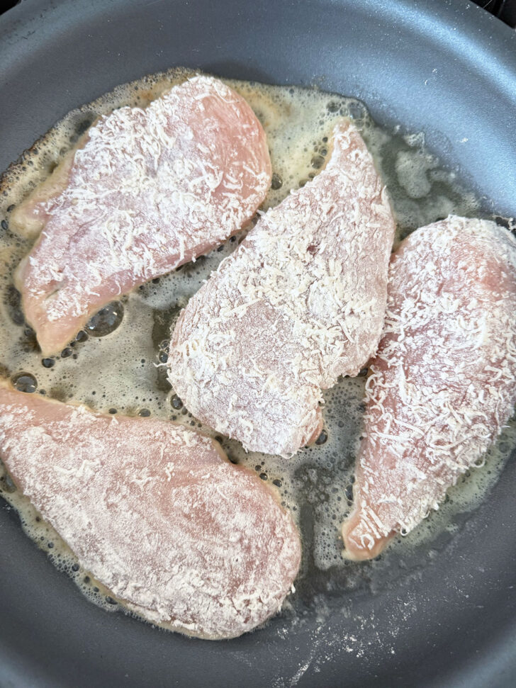 Parmesan-coated chicken cutlets cooking in butter in a skillet.