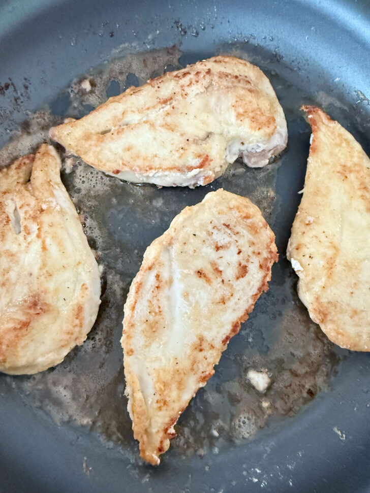 Browned chicken cutlets in a skillet.