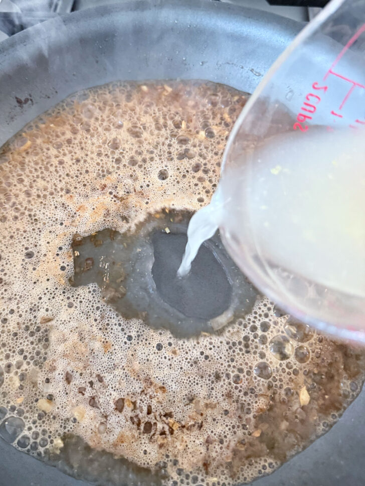 Adding chicken broth to the skillet.