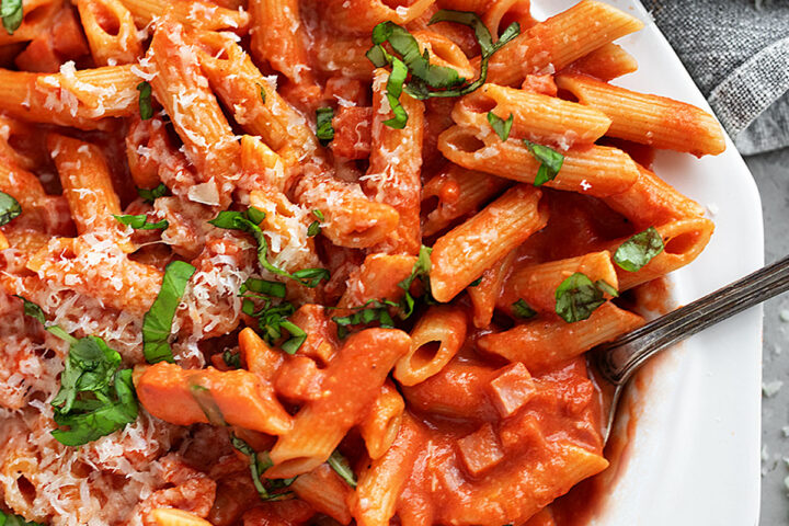 Ham and tomato sauce pasta on a large plate.