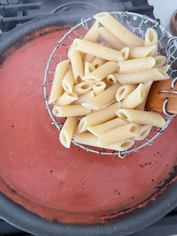 Adding the cooked pasta to the ham and tomato sauce.