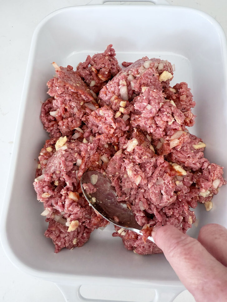 Pressing the meat mixture into a casserole dish.