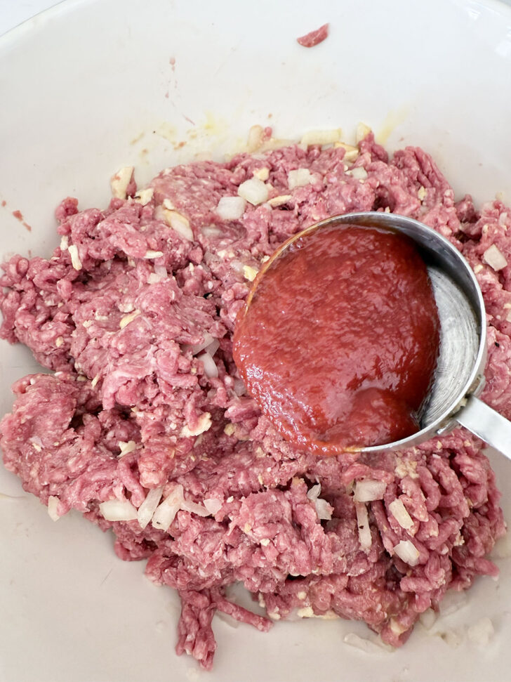 Adding tomato sauce to the meat mixture.