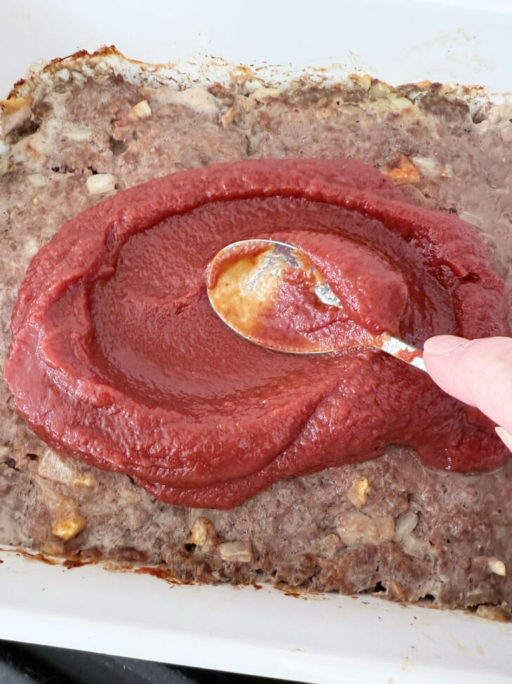 Spreading the tomato sauce over the baked meatloaf mixture.