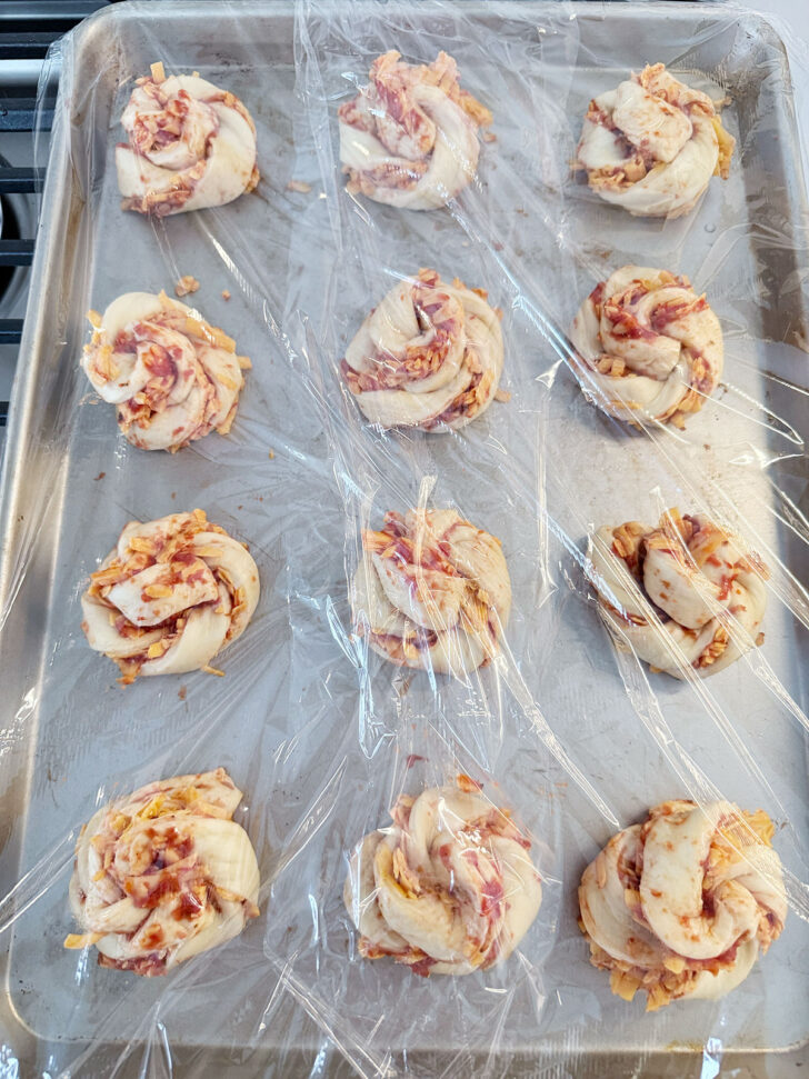 Pizza twists on a baking sheet covered with plastic and set to rise.