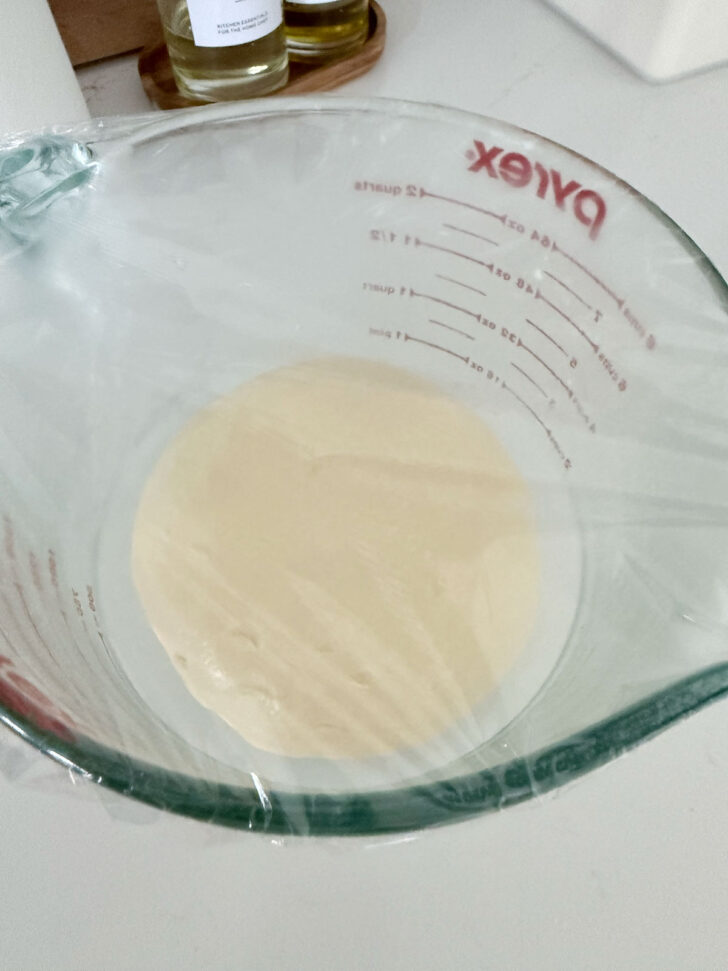 Dough set to rise in a large measuring cup.