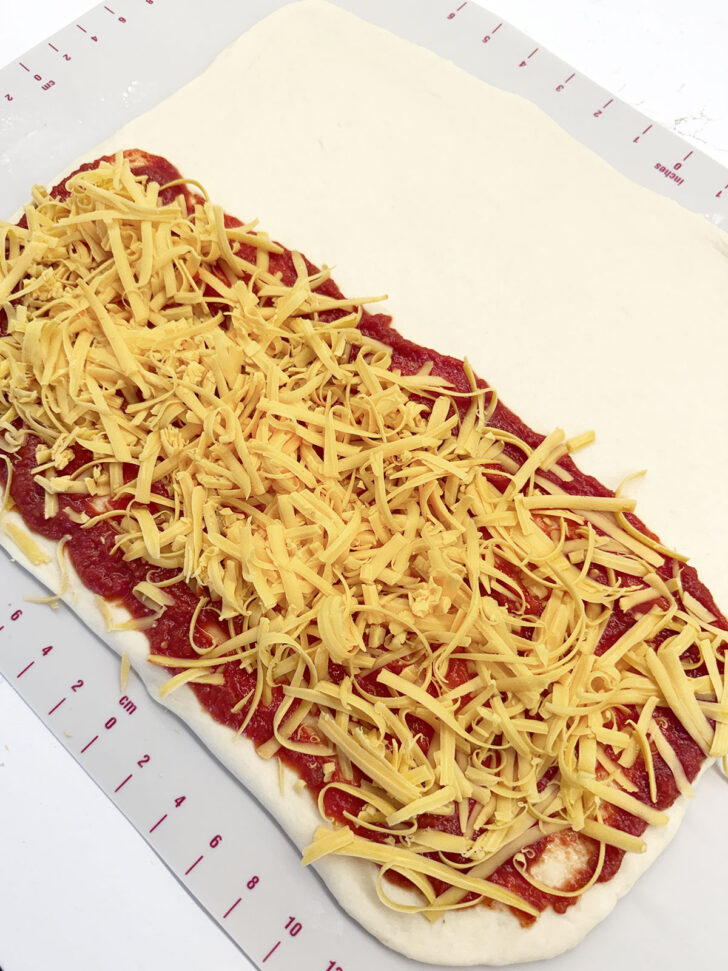 Cheese scattered over the pizza sauce on the rolled dough.