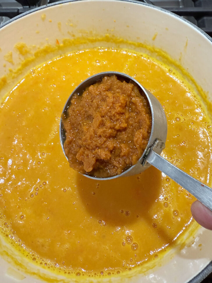 Adding pumpkin puree to the soup pot.
