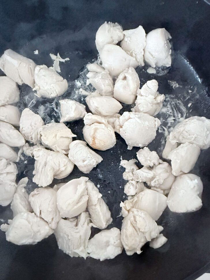 Chicken pieces cooking in a skillet.