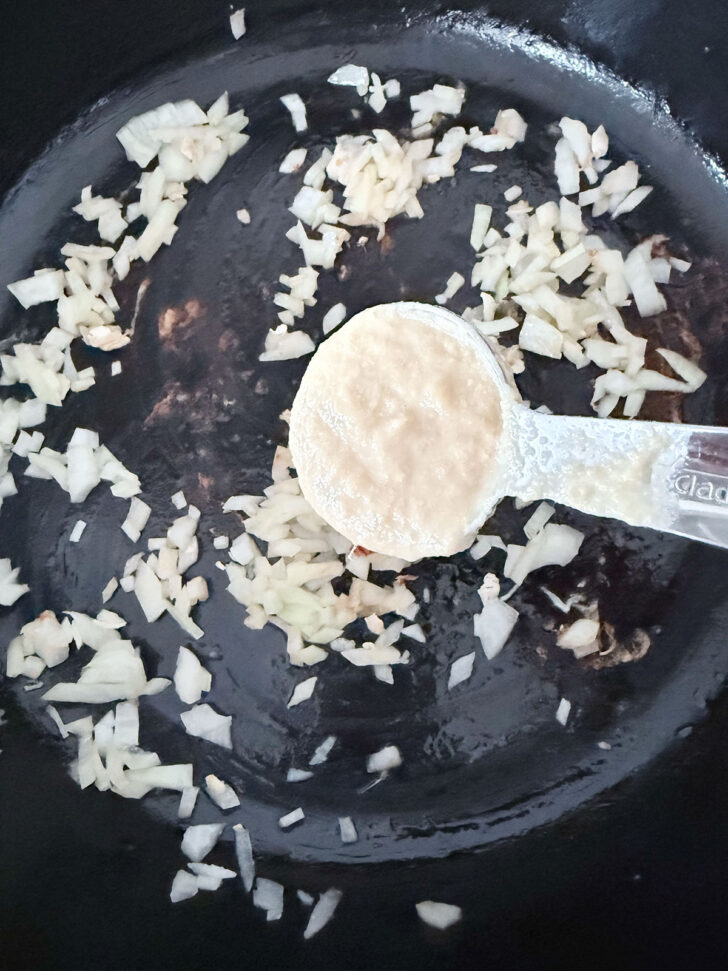 Adding ginger garlic paste to the skillet with the onion.