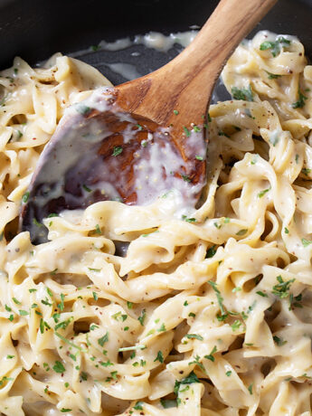 Cafeteria noodles in the skillet with a wooden spoon.