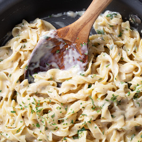 Cafeteria noodles in the skillet with a wooden spoon.