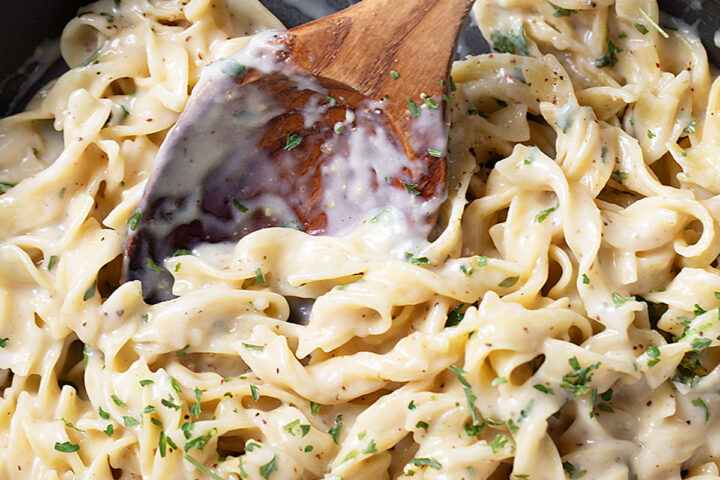 Cafeteria noodles in the skillet with a wooden spoon.
