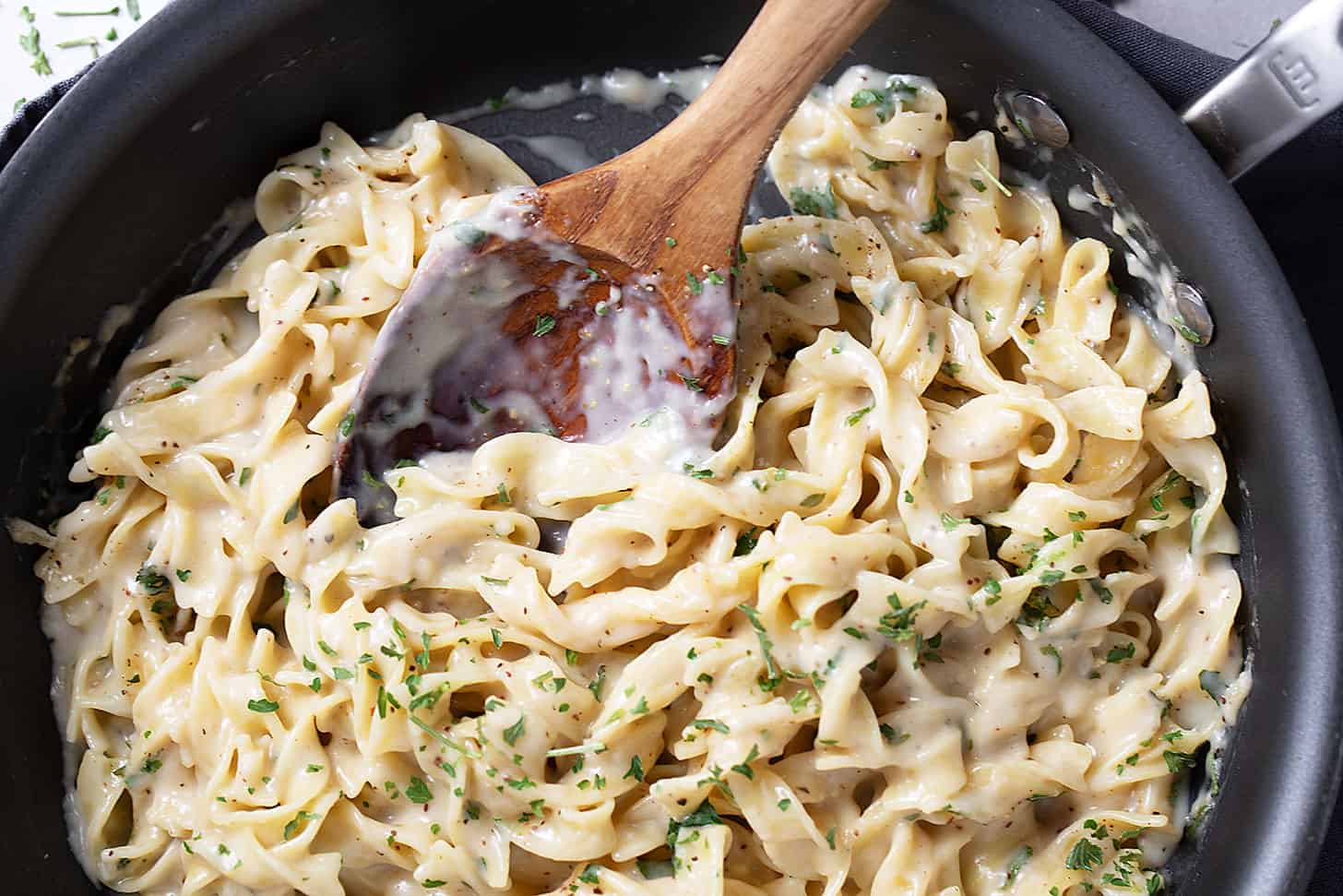 Cafeteria noodles in the skillet with a wooden spoon.