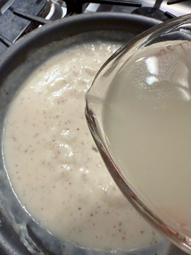 Adding more chicken broth to the skillet.