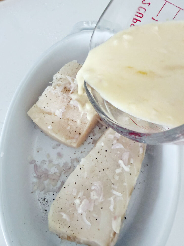 Pouring the creamy lemon sauce over the halibut.
