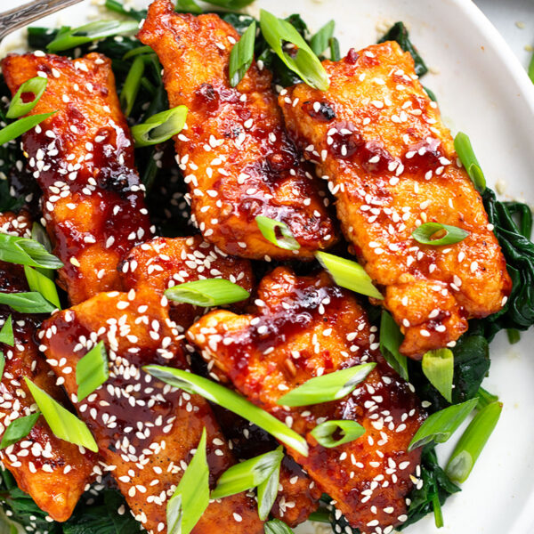 Sticky spicy salmon on a serving platter with cooked spinach.