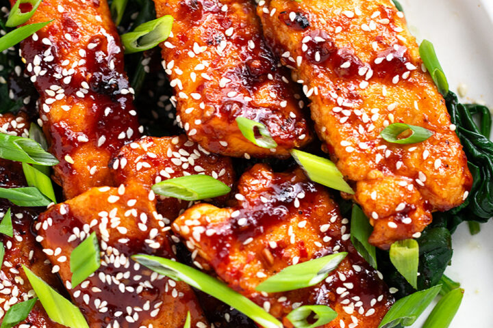 Sticky spicy salmon on a serving platter with cooked spinach.