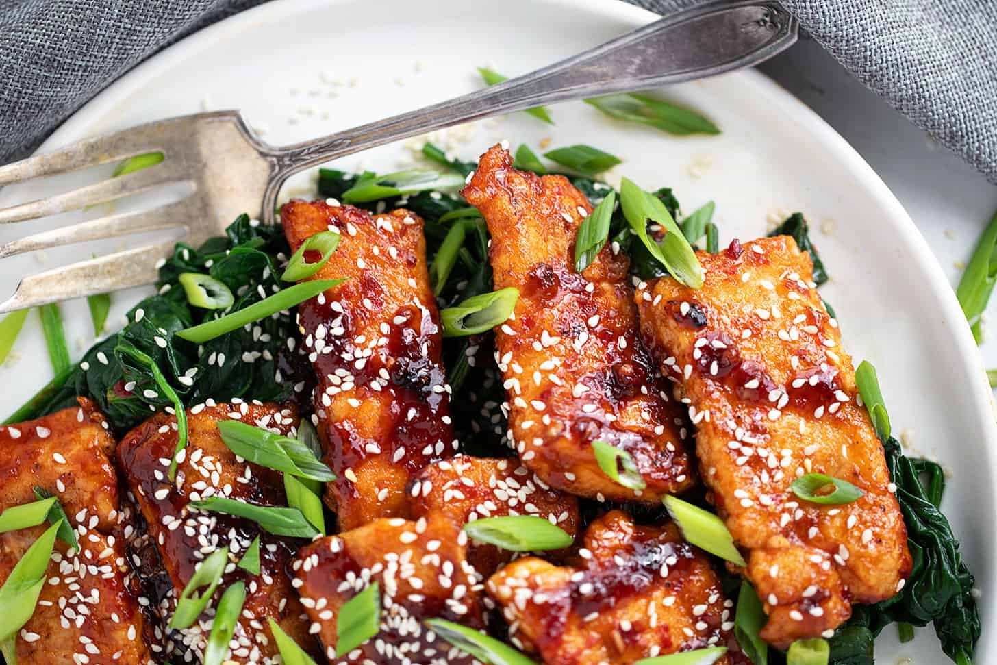 Sticky spicy salmon on a serving platter with cooked spinach.