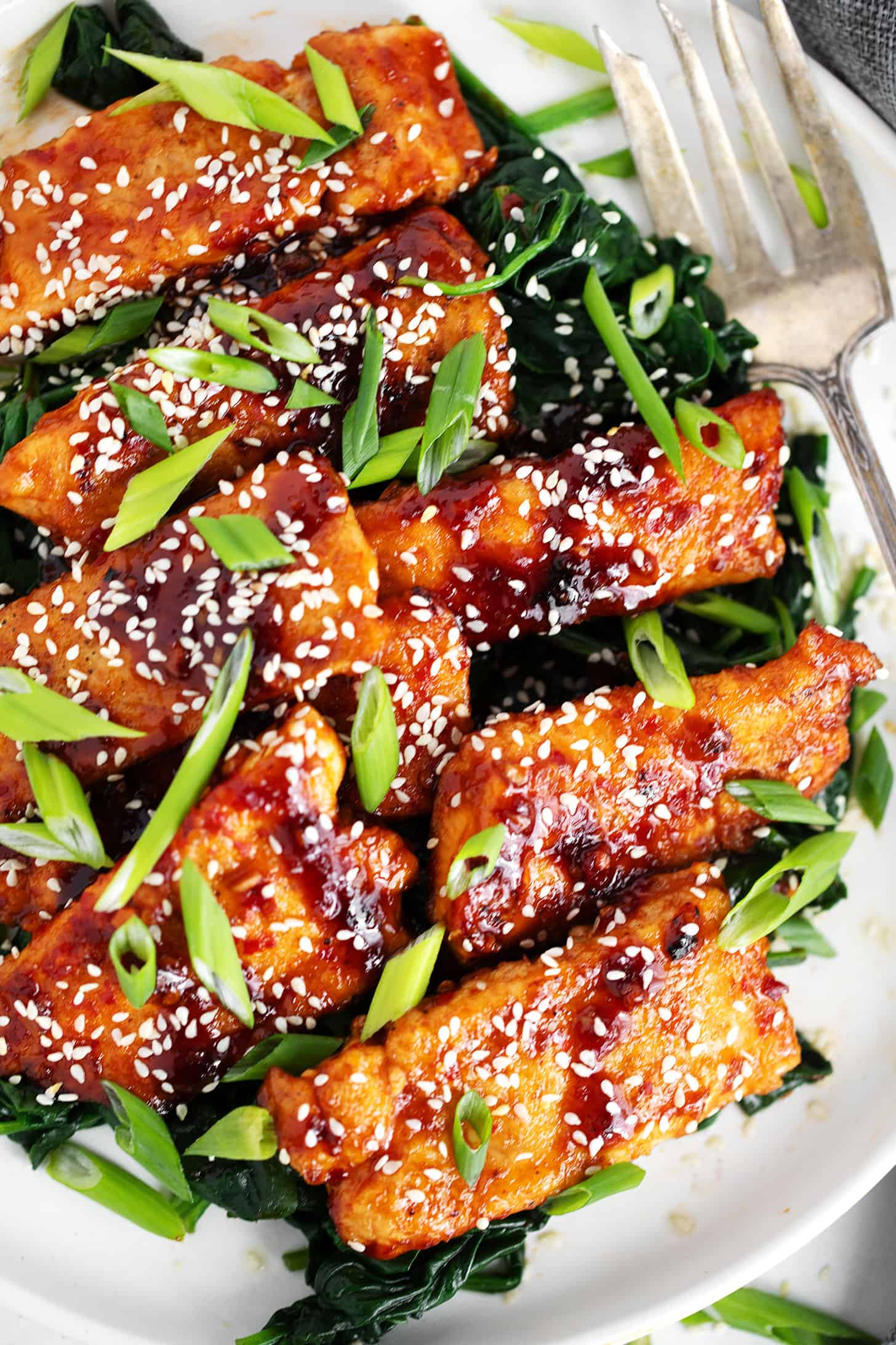 Sticky spicy salmon on a serving platter with cooked spinach.