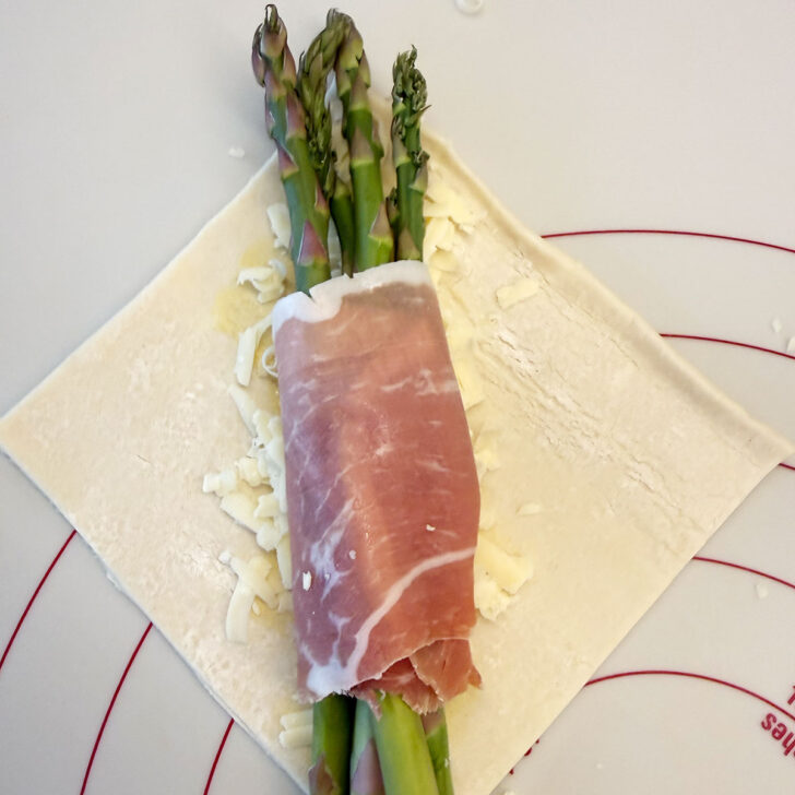 Prosciutto-wrapped asparagus spears on top of shredded cheese, on a puff pastry square.