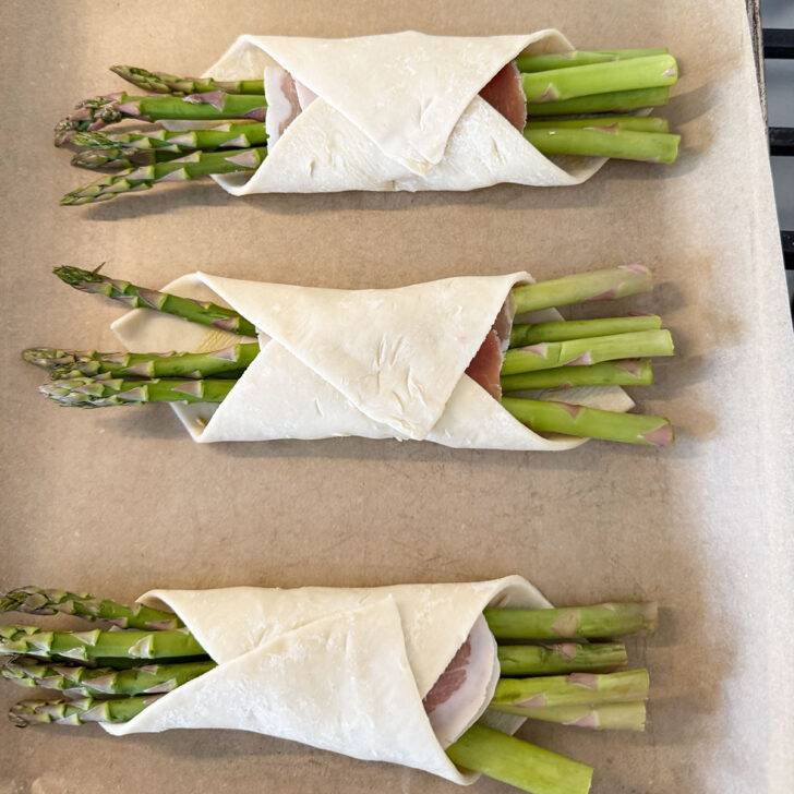 Puff pastry wrapped asparagus on a baking sheet.