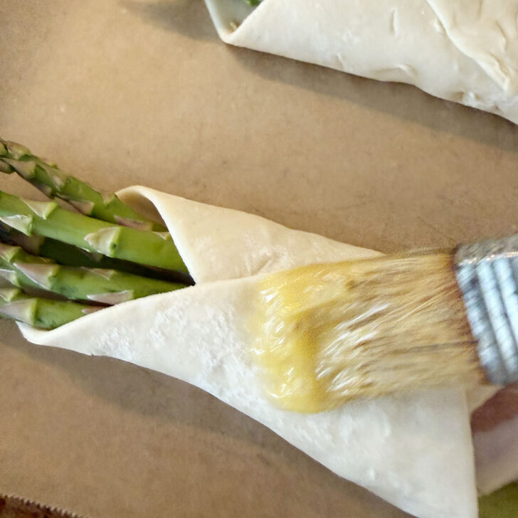 Brushing the puff pastry with egg wash before baking.